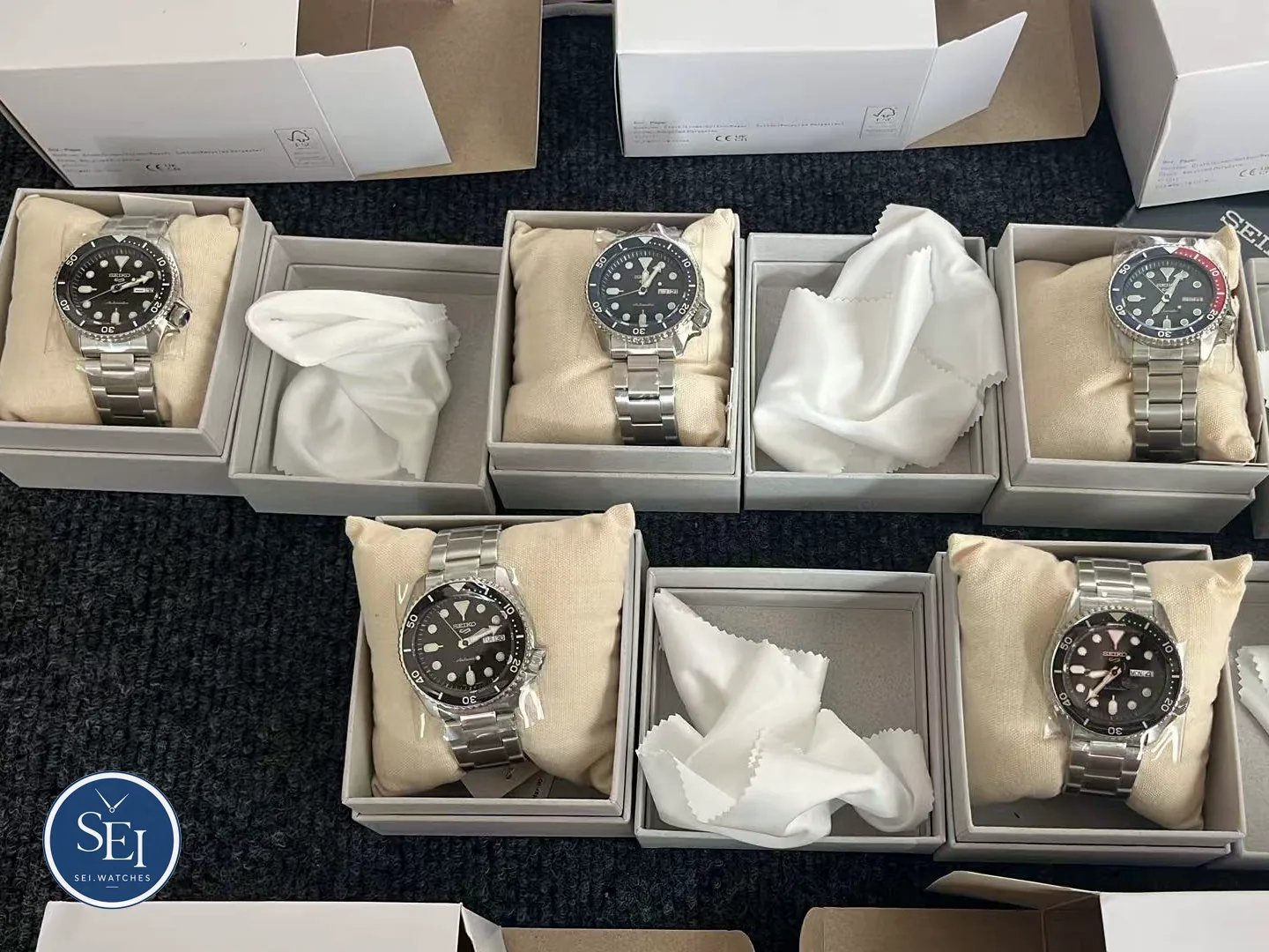 Cinq Seiko 5 Sports neuves sous film protecteur, chacune dans son écrin avec sa chamoisine